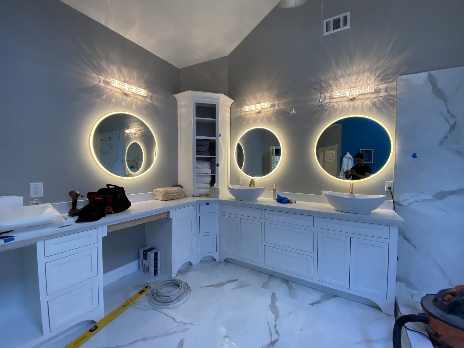 TGP Home Services — luxury primary bathroom remodel in progress with triple backlit round mirrors, dual vessel sinks, and marble flooring