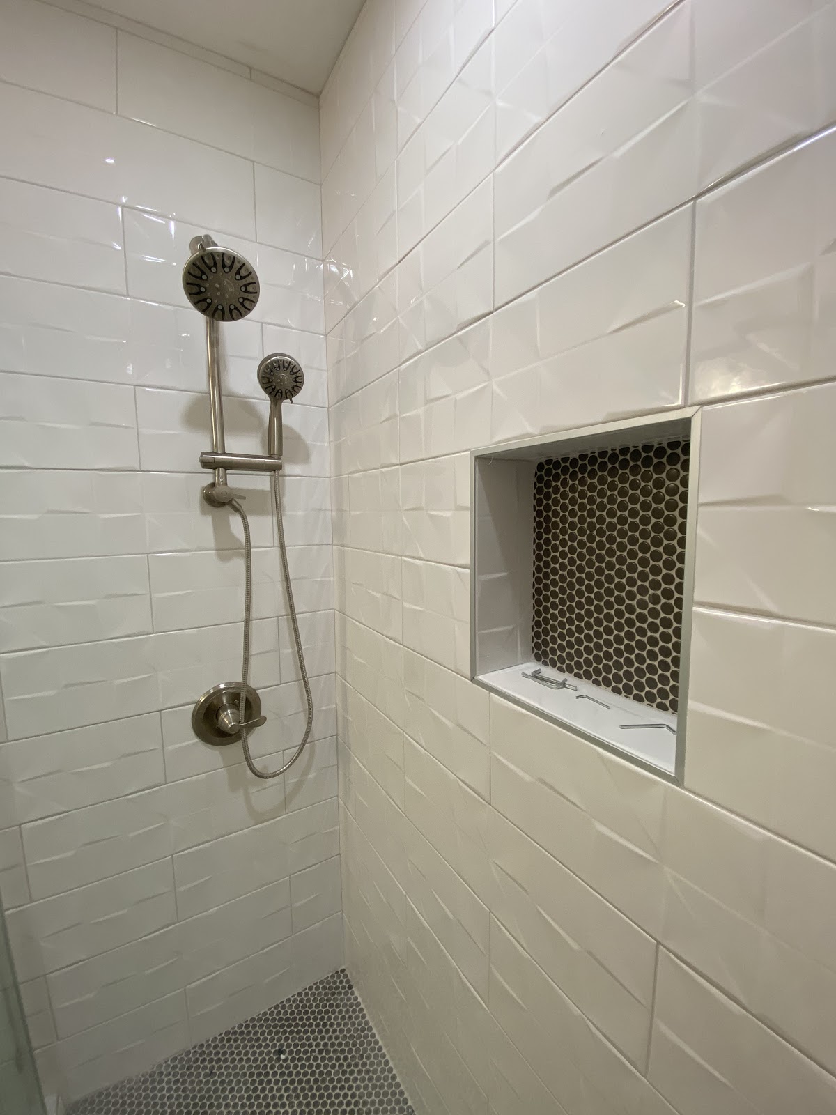 TGP Home Services — finished white subway tile shower with penny-mosaic niche and brushed-nickel rail shower fixture